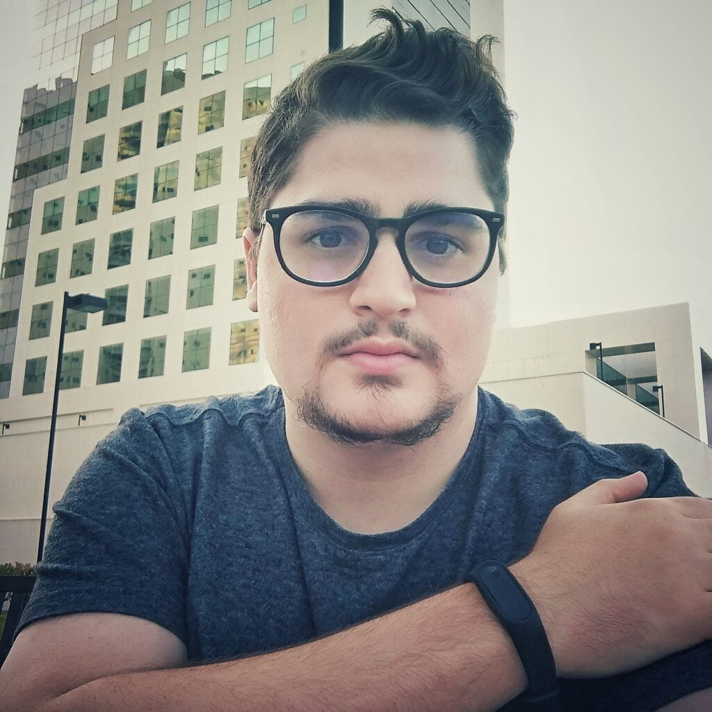 Empreendedor pensativo com óculos sentado ao ar livre com edifícios de escritórios ao fundo, demonstrando seriedade e determinação.