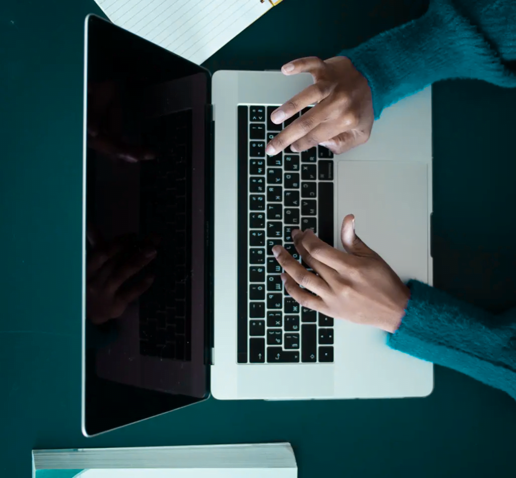 Mãos trabalhando em um laptop sobre uma mesa escura.