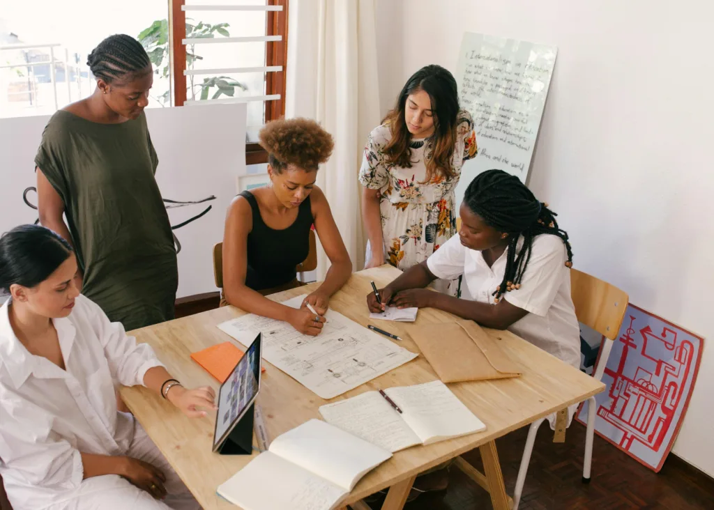 Equipe colaborando em uma mesa com dispositivos e esboços para criar conteúdo visual e estratégias de marketing digital.